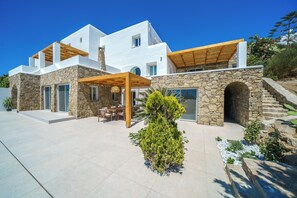 Ein modernes, zweistöckiges Haus mit Steinwänden, einer Holzpergola und einer Terrasse mit Gartenmöbeln.