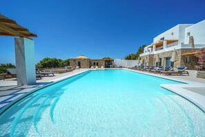 Une piscine d’un bleu éclatant, avec des chaises longues et un bâtiment en pierre en arrière-plan.