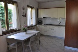 A kitchen with white cabinets, a gas stove, and a sink. There is a dining table with chairs and a potted plant. - Holiday apartment with 2 bedrooms (Malcesine)