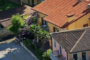 Un quartier résidentiel caractérisé par des toits recouverts de tuiles en terre cuite, une allée pavée et un petit jardin agrémenté de palmiers et de fleurs violettes.