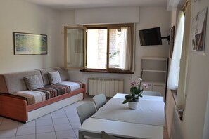 A compact living space with a sofa, a dining table, a potted plant, and a television mounted on the wall. - Holiday apartment with 2 bedrooms (Malcesine)