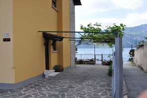 A stone-paved courtyard with a yellow building, a metal gate, and a view of the sea. - Holiday apartment with 2 bedrooms (Malcesine)