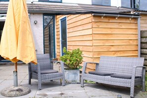 Un espace patio aménagé avec des meubles en osier, une plante en pot et un parasol jaune.