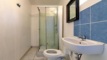 Een badkamer met een douchecabine van glas, een witte wastafel en een toilet.