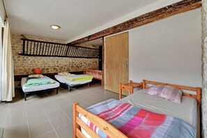 A room with two beds, a wooden ceiling, a stone wall, and a door.