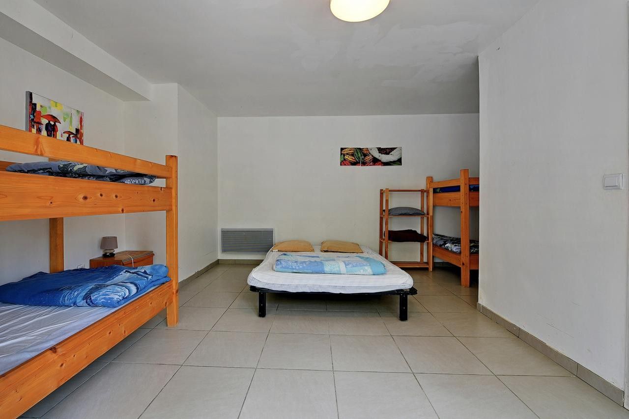 Habitación tipo dormitorio con literas, una cama central con almohadas, una mesita con lámpara y un cuadro colgado en la pared.