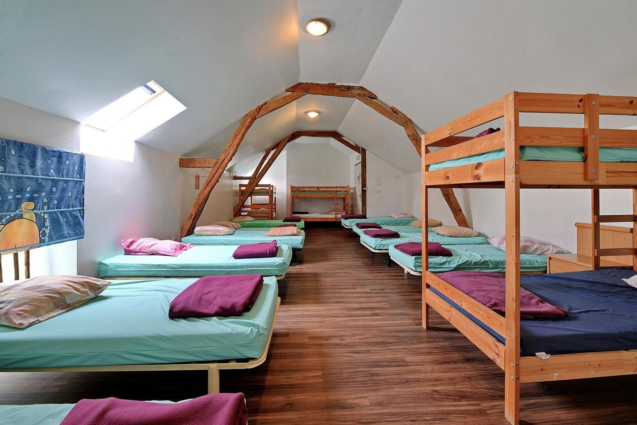 A dormitory room with bunk beds, wooden beams, and a sloped ceiling.