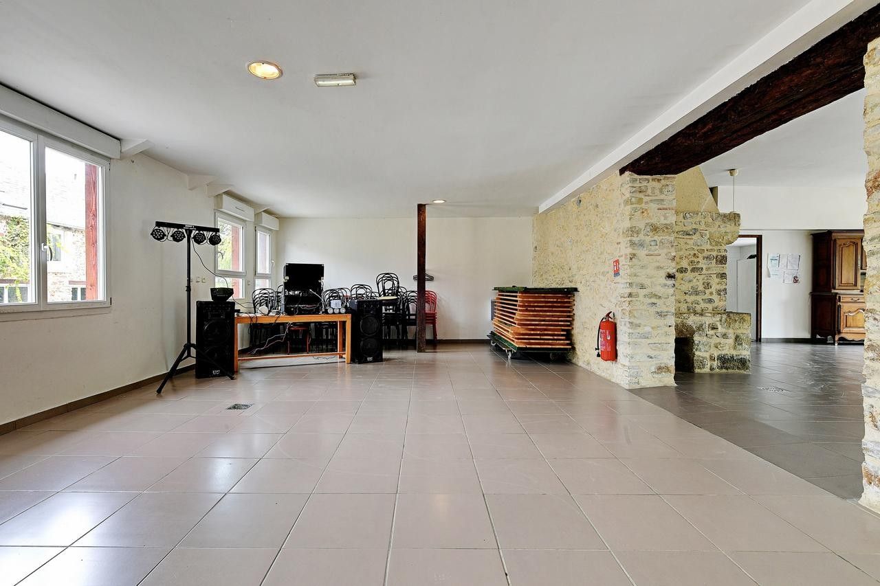 Una habitación amplia con suelo de baldosas, un escenario con equipo musical, una pared de piedra y una puerta que da a otra habitación.