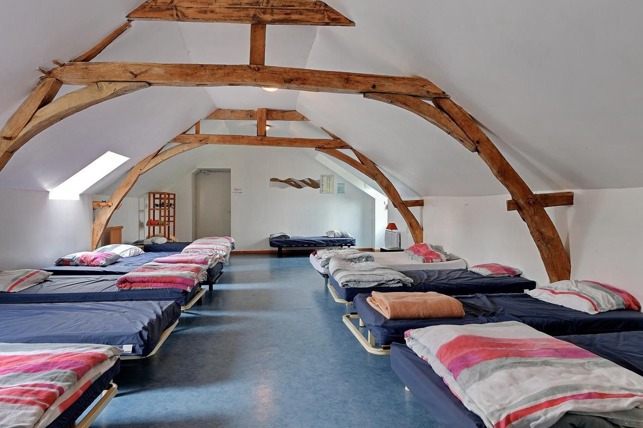 A room with multiple beds arranged in rows, wooden beams on the ceiling, and a skylight.
