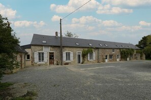 A stone building with multiple windows and doors, a gravel driveway, and a clear sky.