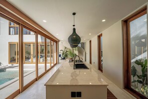 A modern kitchen with a marble countertop, a hanging pendant light, and large windows. - Villa GIGI Balangan (Balangan)