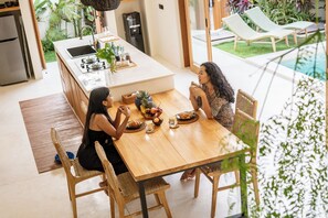 A dining area with a wooden table, two chairs, and a kitchen in the background. - Villa GIGI Balangan (Balangan)