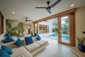 A modern living room with a sofa, ceiling fans, and a view of a pool and outdoor area. - Villa GIGI Balangan (Balangan)