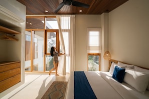 Un dormitorio moderno con una cama grande, un ventilador de techo y vistas a través de un ventanal corredero.