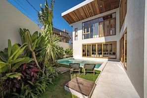 Una casa moderna con piscina, mobiliario de exterior y exuberante vegetación tropical.