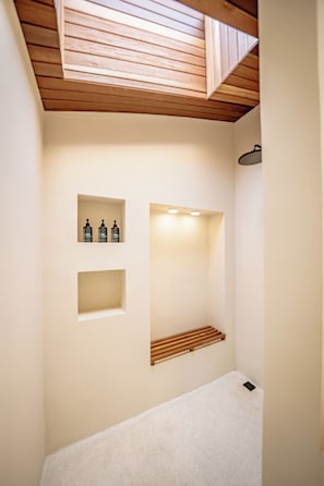 Un baño con tragaluz, ducha y dos repisas con botellas.