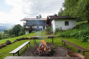A chalet with a fire pit in the foreground, surrounded by picnic tables and a grassy area. - Katharina's Alpine Hut (Mühlbach im Pinzgau)
