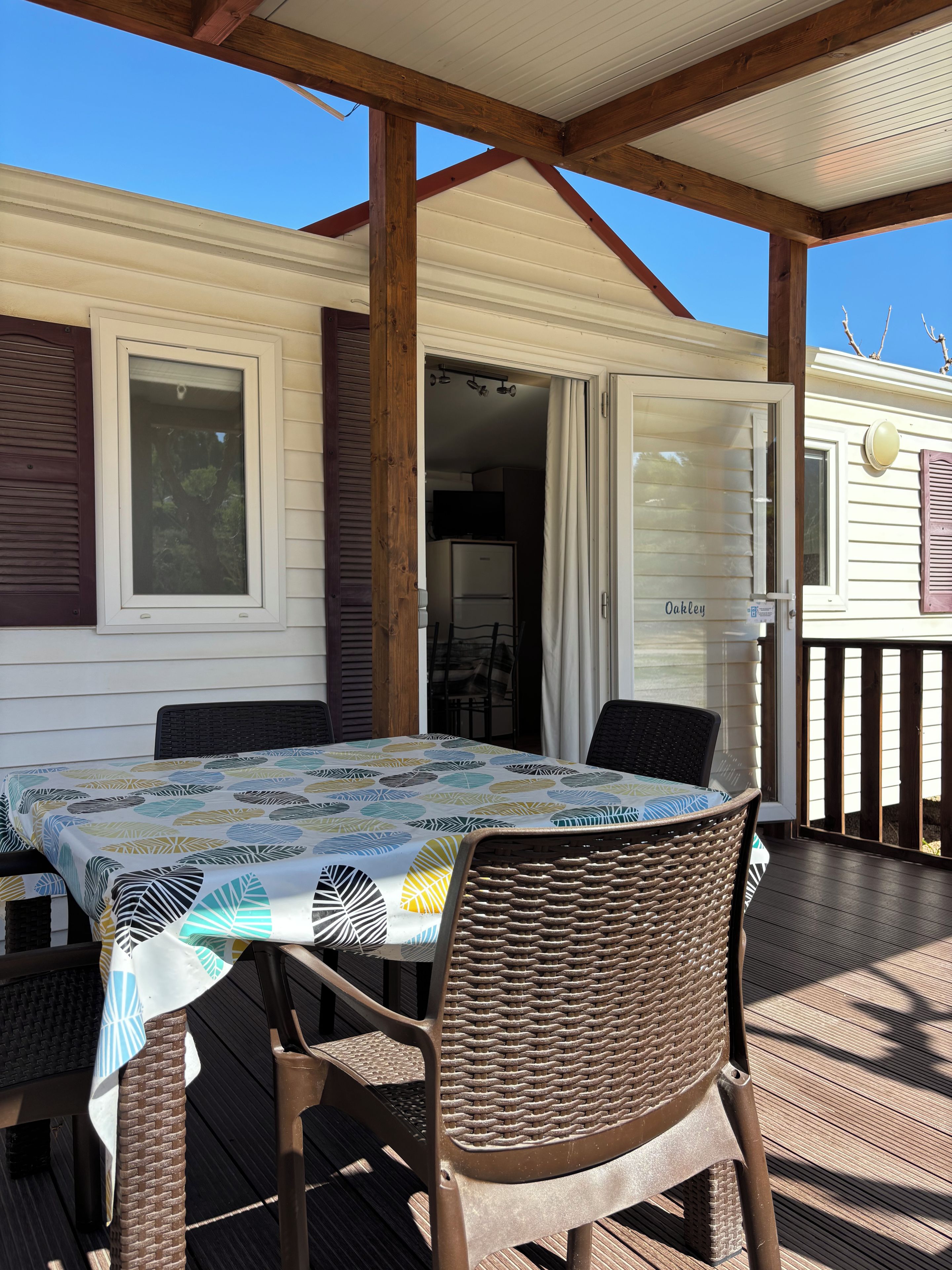 Un patio techado al aire libre con una mesa y sillas, una terraza de madera y vistas a una casa con placa identificativa.