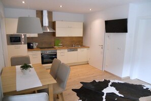 A compact kitchen with modern appliances, a dining area with a table and chairs, and a large black and white cow hide rug. - Holiday apartment with 2 bedrooms (Eben im Pongau)