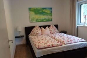 A bedroom with a bed, a nightstand, a lamp, a painting, and a window with curtains. - Holiday apartment with 2 bedrooms (Eben im Pongau)