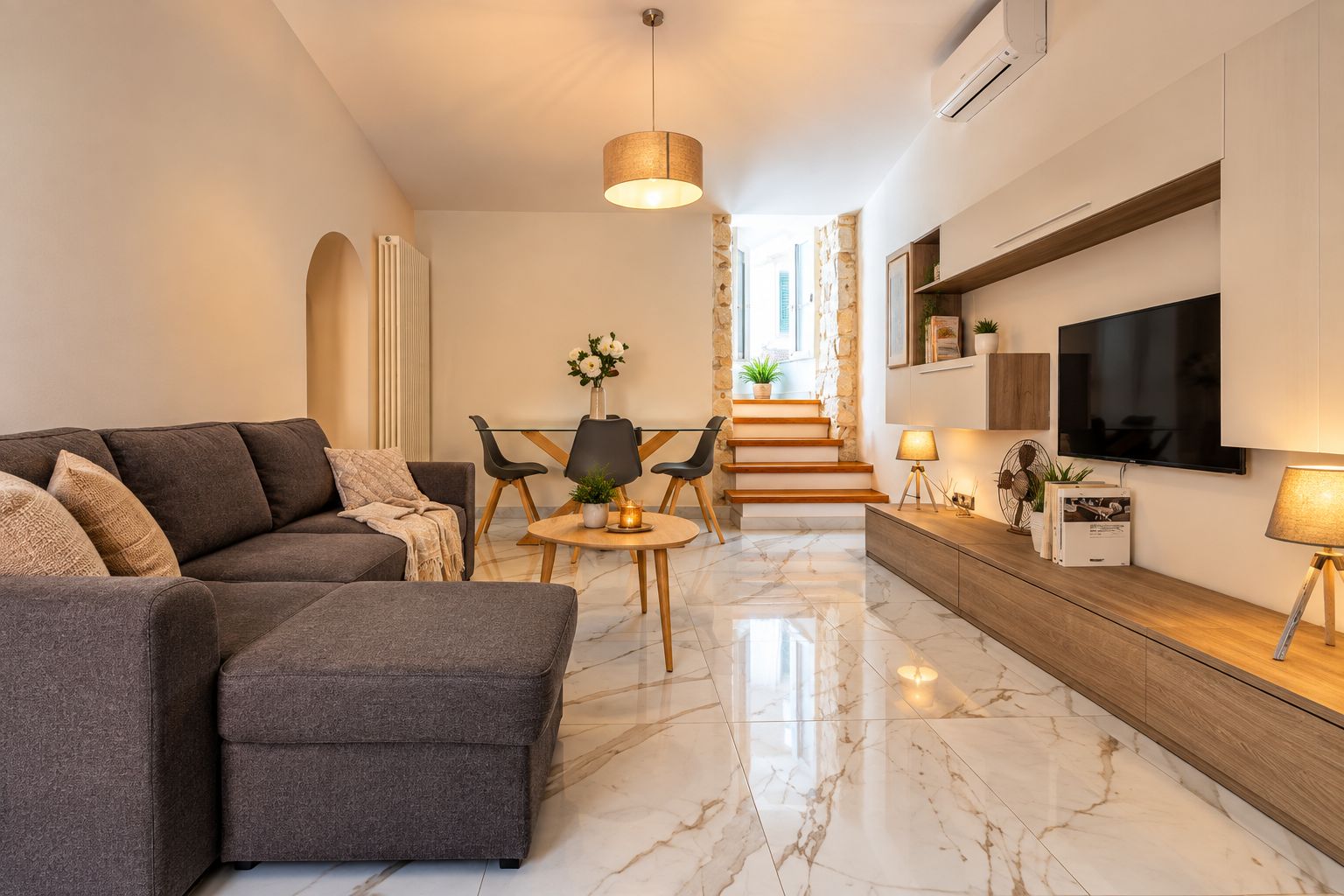 Una sala de estar moderna con un sofá, una mesa de comedor y un televisor montado en la pared.