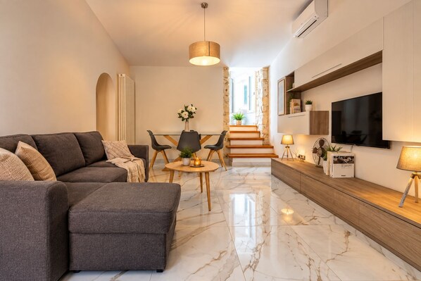 A modern living room with a sofa, a dining table, and a TV mounted on the wall.
