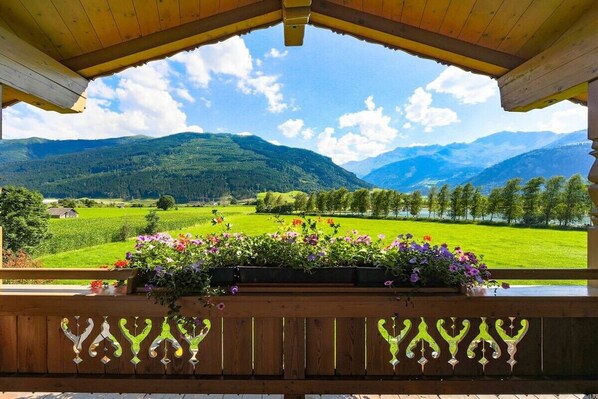 Un balcon en bois offrant une vue sur un paysage montagneux, agrémenté d’une jardinière remplie de fleurs violettes.