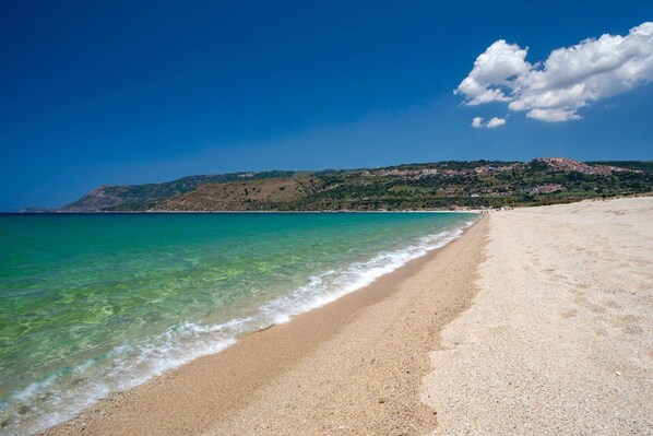 Una playa con agua turquesa cristalina, una orilla arenosa y un paisaje montañoso al fondo.