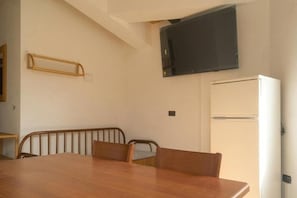 A room with a wooden dining table, chairs, a flat-screen TV mounted on the wall, and a white refrigerator. - Apartment with shared pool near the sea (Nicotera (VV))
