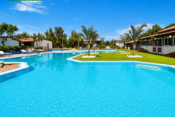 Una gran piscina con agua cristalina azul, rodeada de palmeras y sillas de descanso.