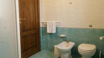 Ein Badezimmer mit Holztür, einem Bidet, einer Toilette und einem auf einem Wäscheständer hängenden Handtuch.