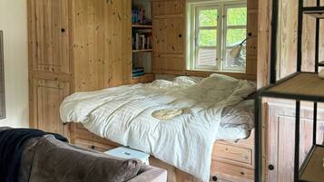 A bedroom with a bed, wooden walls, a window, and a bookshelf.