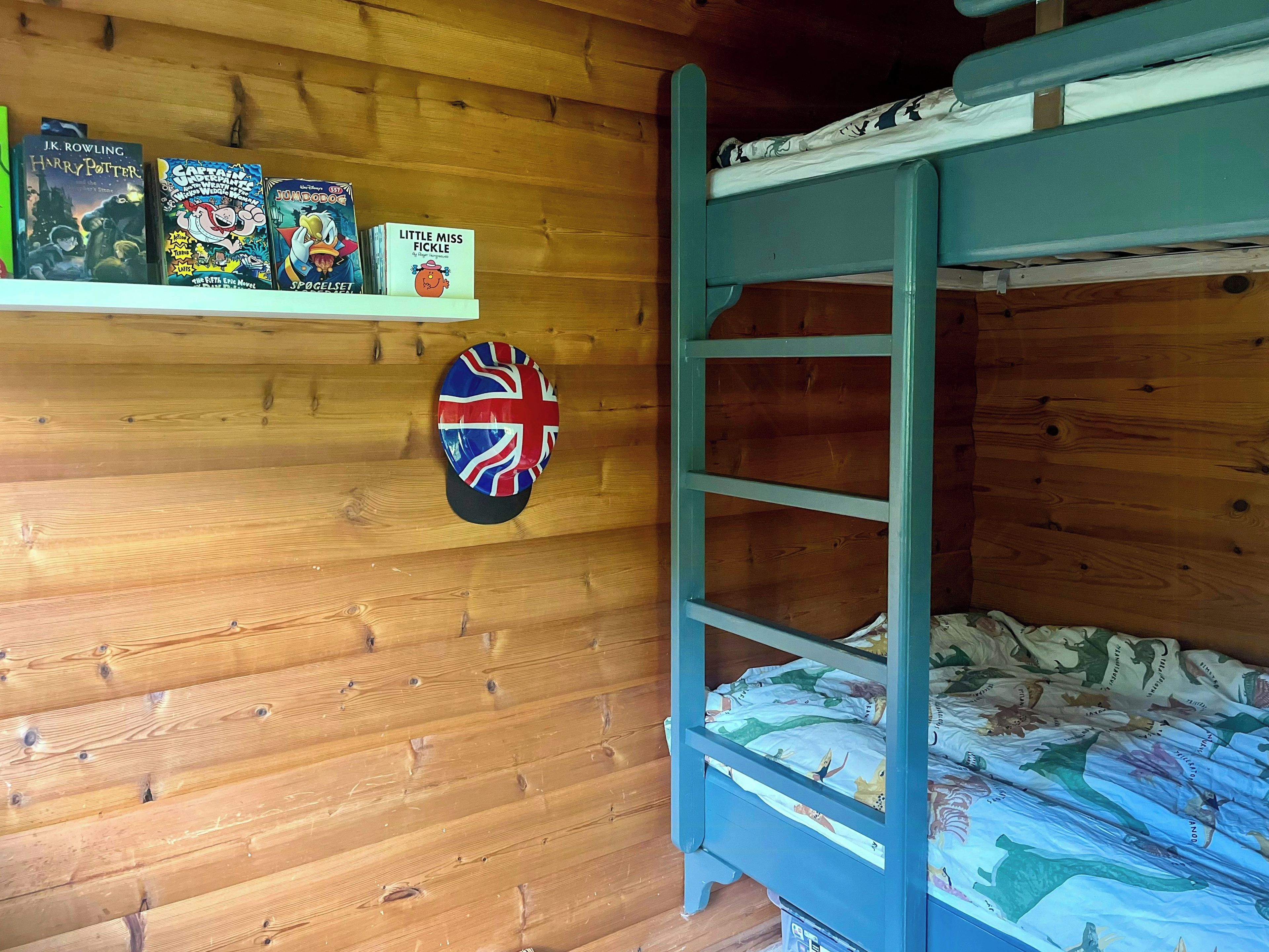 A bunk bed with a blue frame, a shelf with books, and a flag decoration on the wall.