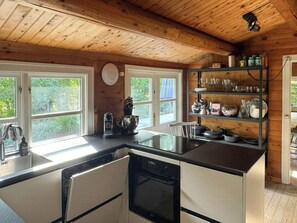 Una cocina con vigas de madera, lavavajillas, pileta y ventana con vista a la vegetación.