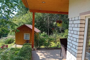 Eine Holzhütte mit rotem Dach, einer Laube und einem Garten mit verschiedenen Pflanzen und einem Stuhl.