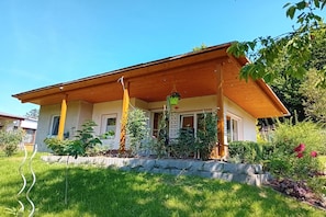 Ein zweistöckiges Haus mit einer Holzveranda, einer Steinmauer und verschiedenen Pflanzen.