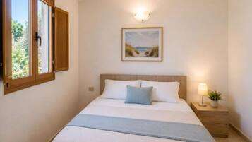 Une chambre à coucher avec un lit, une table de chevet, une lampe, une fenêtre avec des rideaux et un tableau au mur.