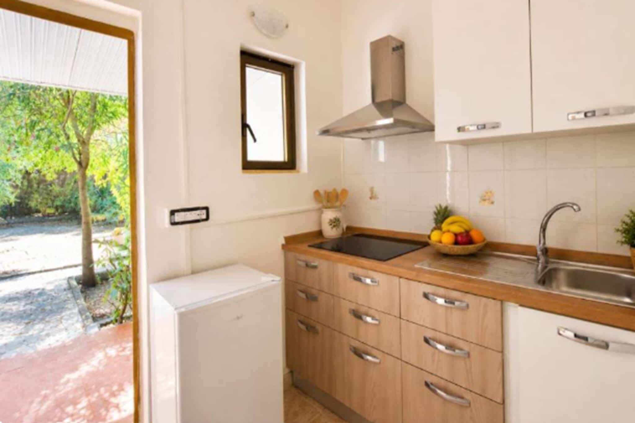 Une cuisine compacte dotée d’un réfrigérateur encastré, de meubles de rangement en bois, d’un évier en acier inoxydable et d’un panier à fruits posé sur le plan de travail.