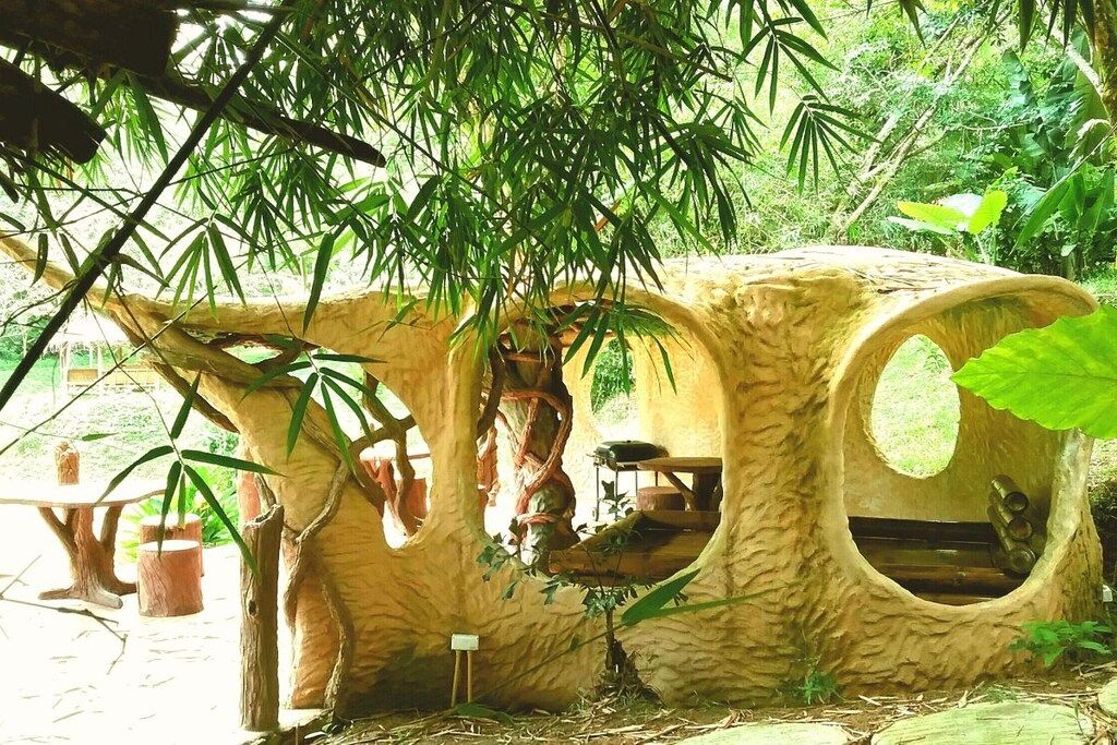 Une cabane dans les arbres avec une fenêtre ronde, une petite table et un banc.