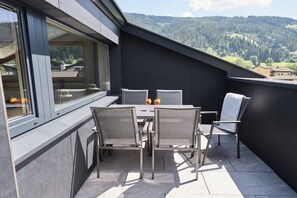 A balcony with a table and chairs, a window, and a view of a forested mountain range. - Apartment in Eben with swimming pool (Eben)