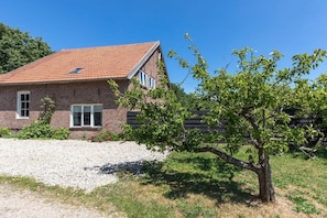 Une maison en briques avec un toit en tuiles, une allée en gravier et un arbre au premier plan.