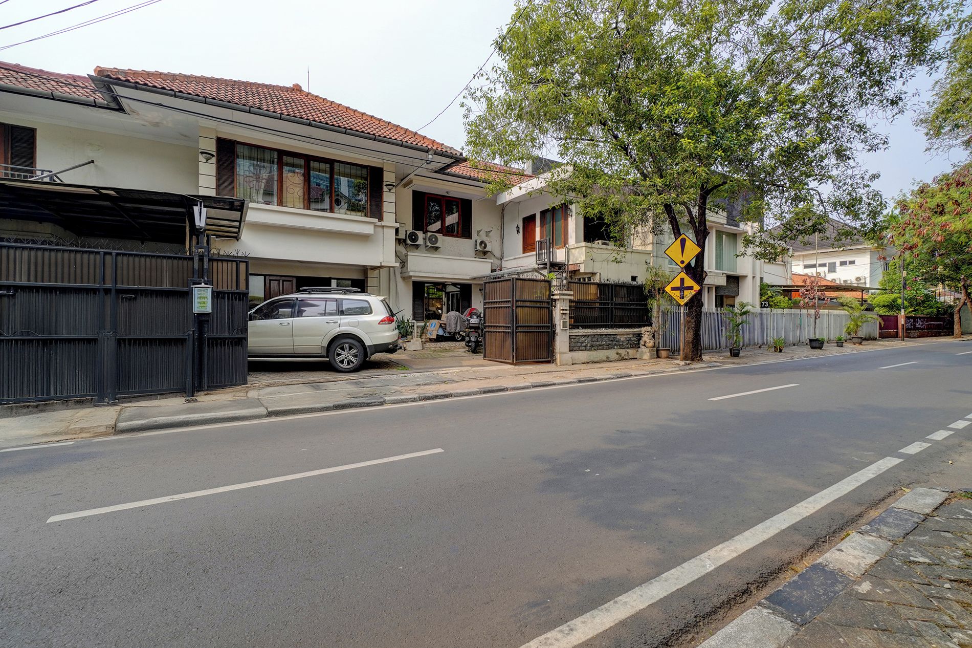 Una calle residencial con casas, un coche estacionado y un paso de peatones.