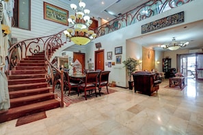 A grand staircase leading to a second floor, a dining area with a table and chairs, and a living room with a sofa and a coffee table. - Cassa Dharmawangsa By ARBA (Jakarta)
