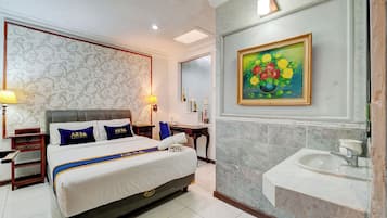 Habitación de hotel con cama, mesitas de noche, lámpara, un cuadro y baño con lavamanos y espejo.