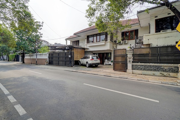 Una calle residencial con casas, un camino de entrada con portón y un automóvil estacionado.