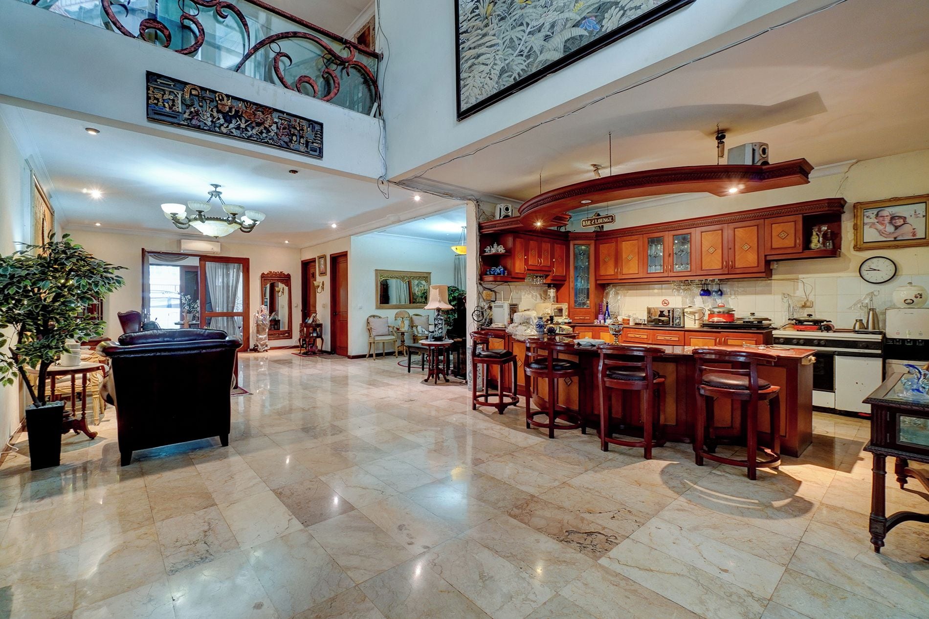 A spacious living area with a high ceiling, a kitchen with bar/lounge area, and a dining space with multiple chairs.