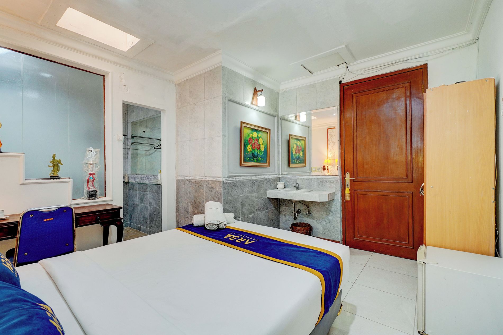 Una habitación de hotel con una cama, un escritorio, una silla, ducha, lavamanos y una puerta.