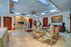 A spacious living room with a glass-top dining table surrounded by chairs, a ceiling fan, and a large painting on the wall. - Cassa Dharmawangsa By ARBA (Jakarta)