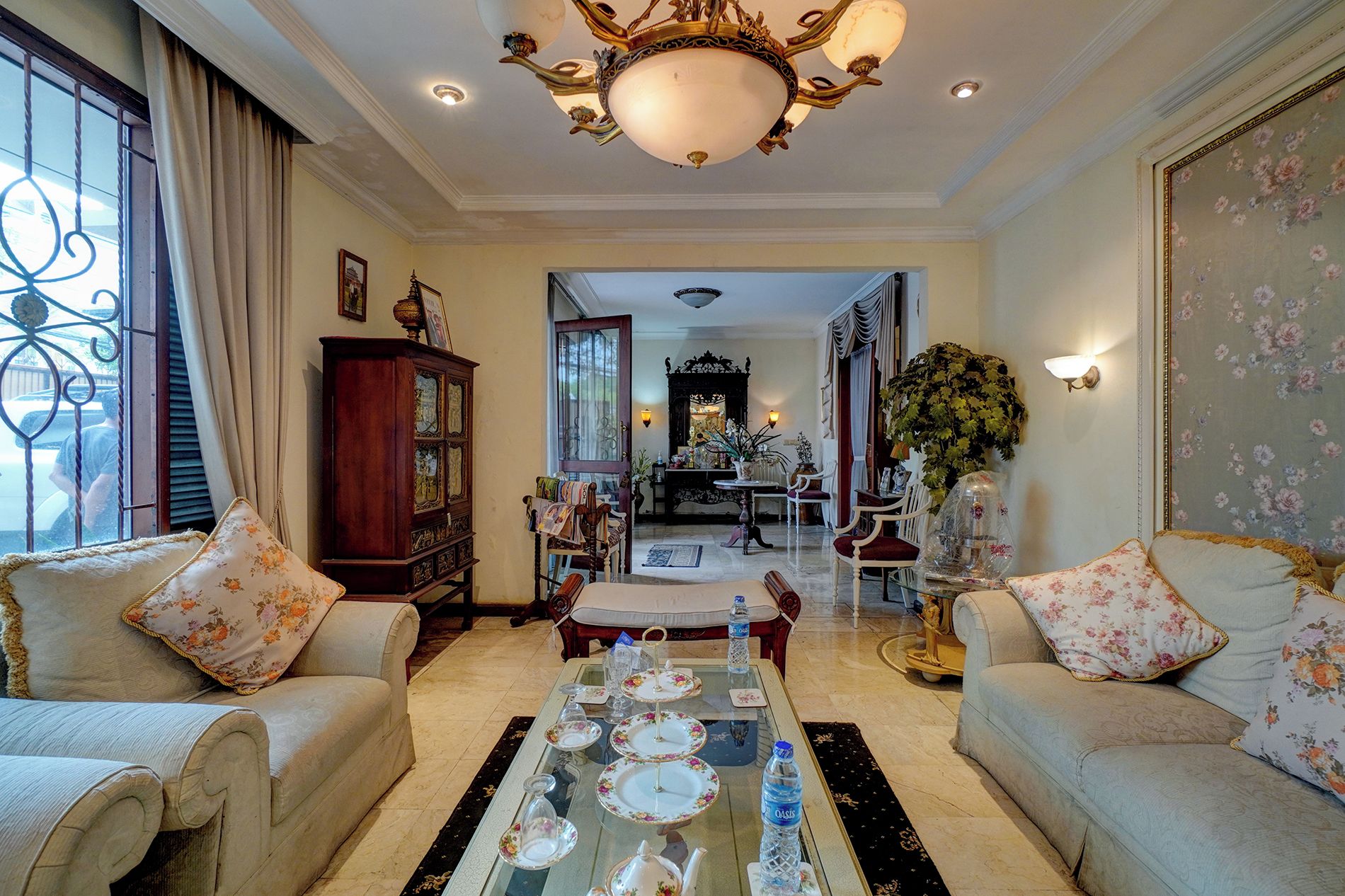 Un salón amplio con una gran araña, una zona de comedor con una decoración floral en la mesa, y vistas a un comedor con un espejo y una araña.