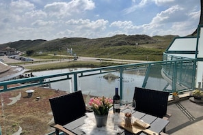 Une terrasse avec une table dressée pour deux personnes, offrant une vue sur une étendue d’eau et un paysage vallonné.